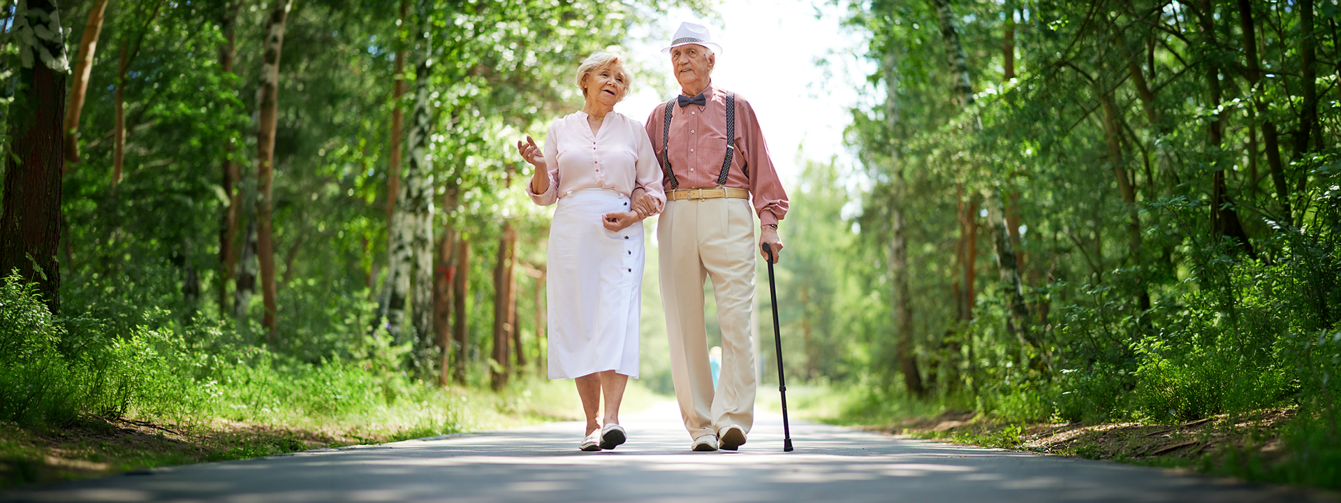 elderly couple walking on a forest path with a walking cane